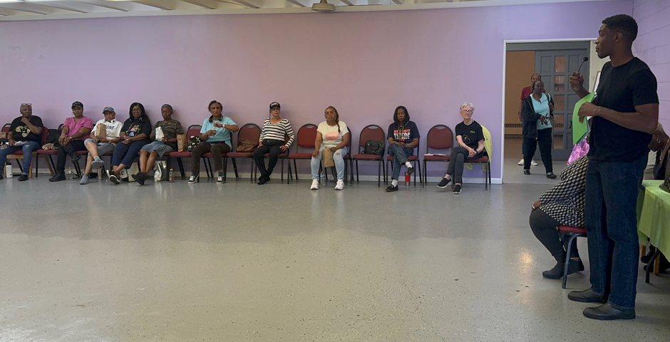 Cova co-founder Jordan Ibe speaking to a seated group at a community line dancing class